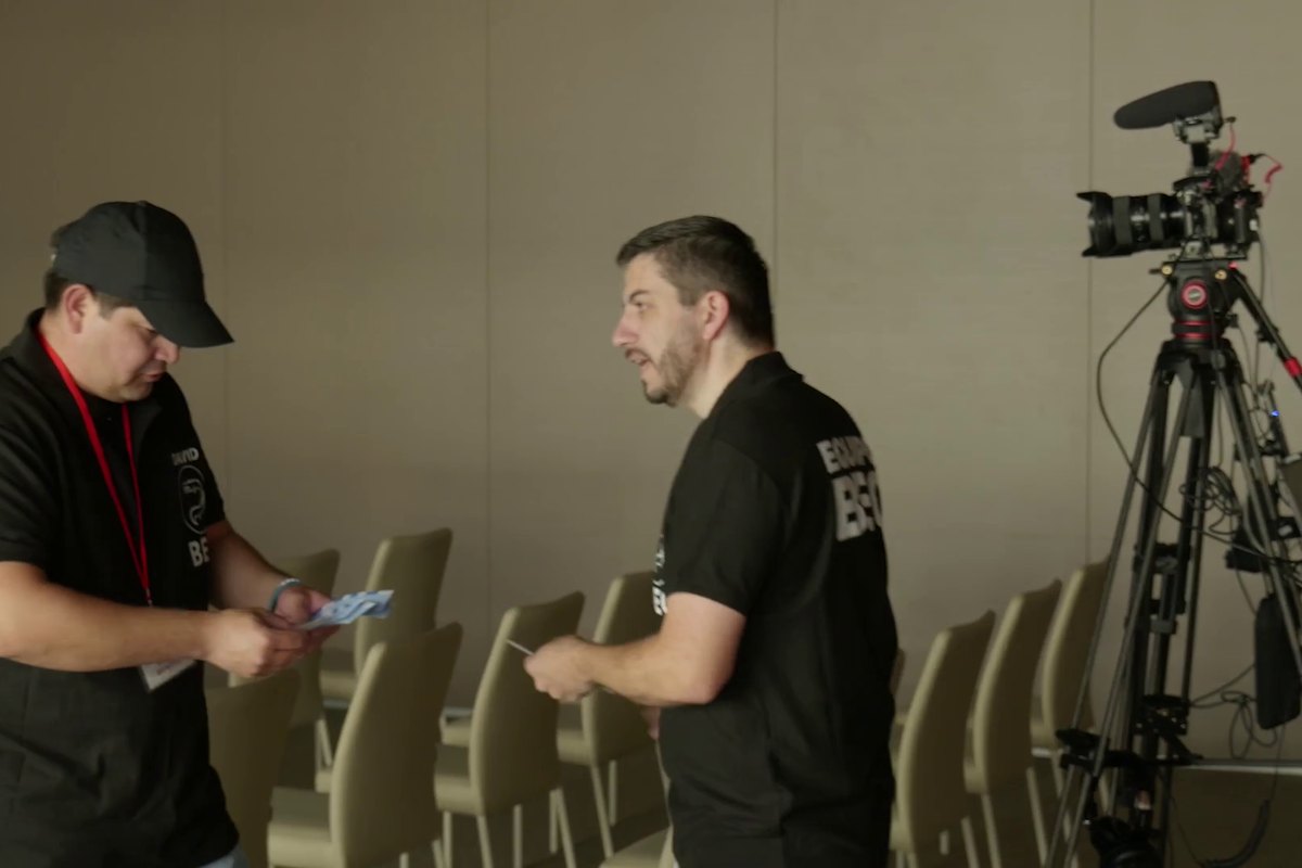 Dos personas del equipo de BEC repasan una lista junto a la cámara del evento, con la sala todavía vacía